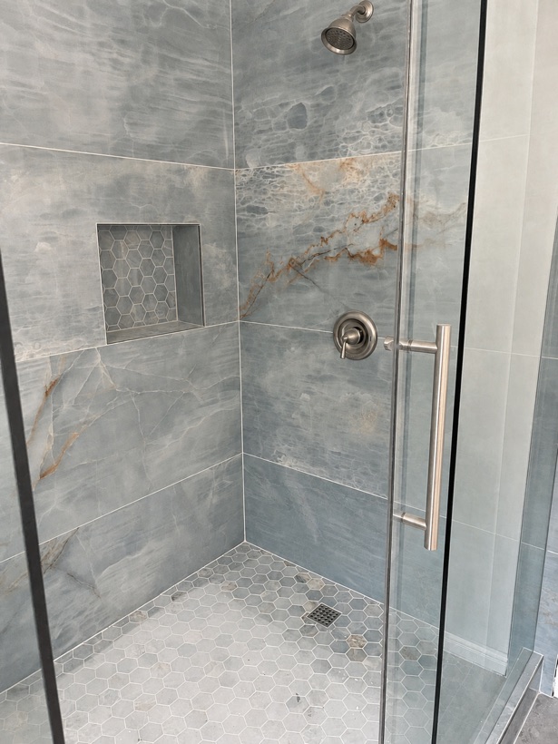 Walk-in shower clad in blue onyx-look marble porcelain with a recessed hexagon mosaic niche
