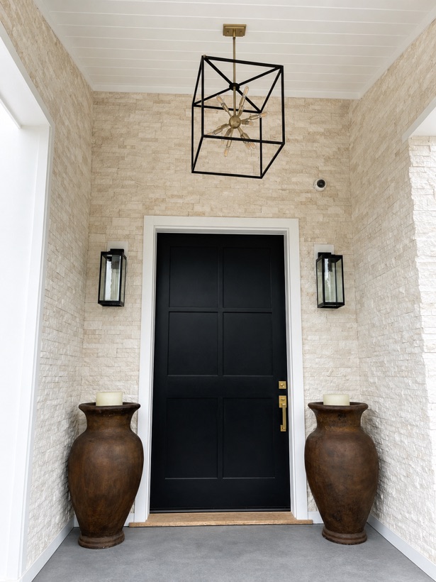Covered front entry porch clad in white stacked stone ledger panel with a dark door and lanterns