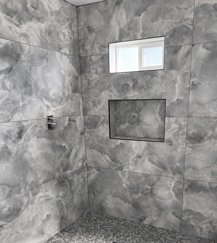 Dramatic gray marble shower with a pebble mosaic floor and two recessed niches