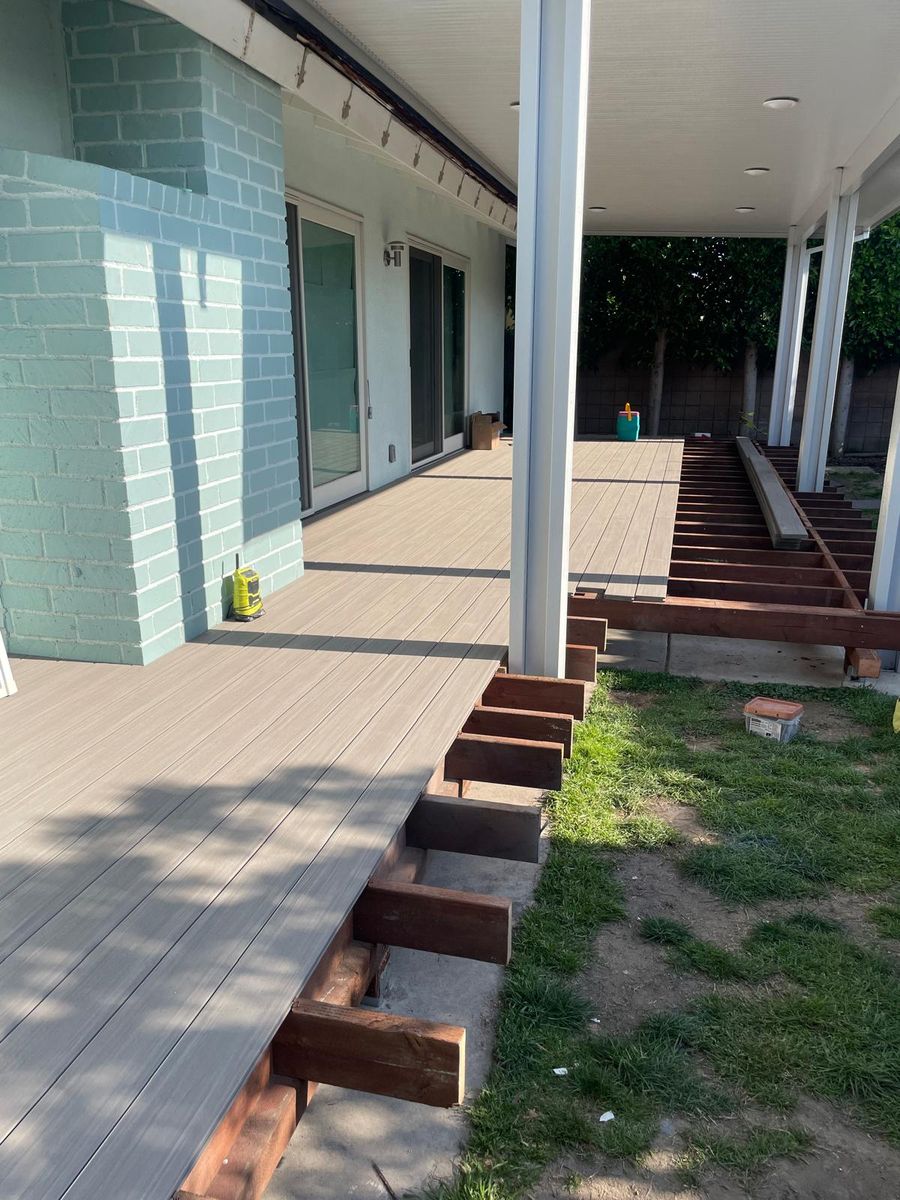 Composite deck with hardwood step treads under construction alongside a tiled exterior wall