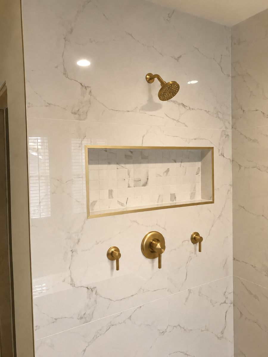 White marble-look shower wall with a recessed niche framed in brushed gold trim and matching gold fixtures