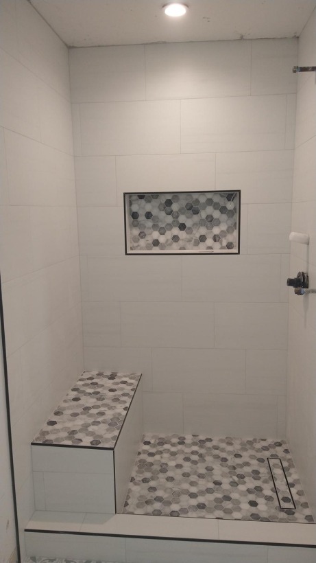 Shower pan with a linear drain, pebble mosaic floor and a built-in bench